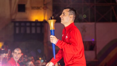 A smiling young man carrying a torch in his left hand.