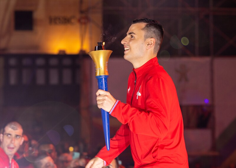 A smiling young man carrying a torch in his left hand.