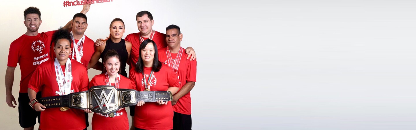 School of Strength trainers and athletes standing together in a group holding a WWE championship belt. 