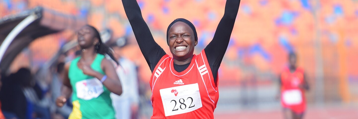 Young women running on a track with her arms raised in victory. 