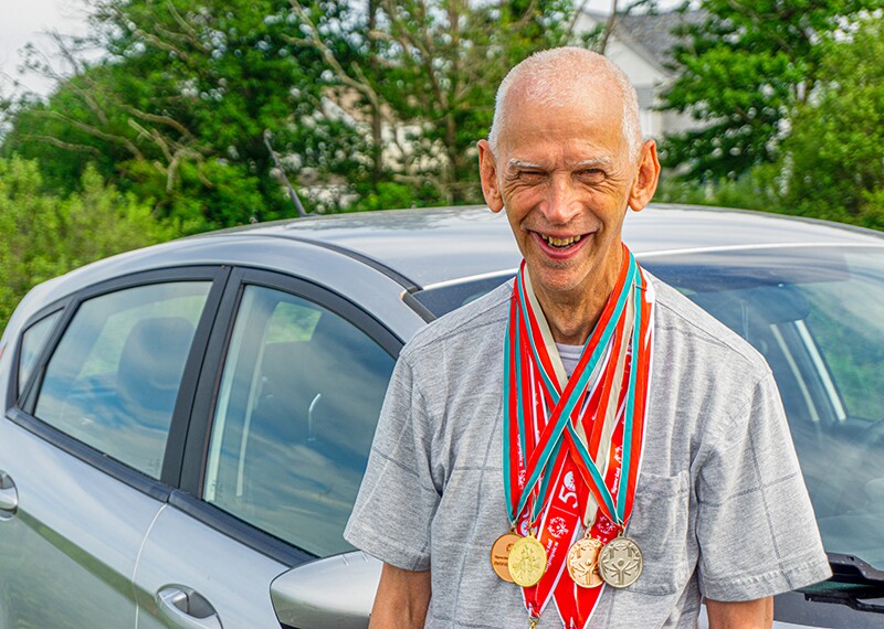 Athlete with medals standing outside in front of a car. 