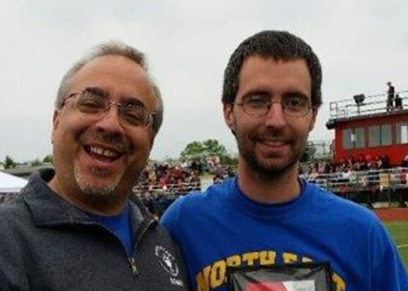 Two men stand on a football field and pose for a photo. 