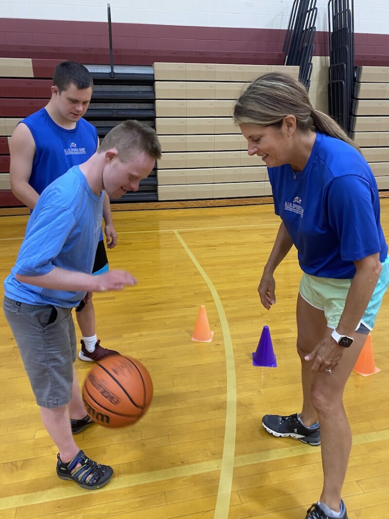 A Special Olympics athlete dribbles a basketball while his coach watches. 