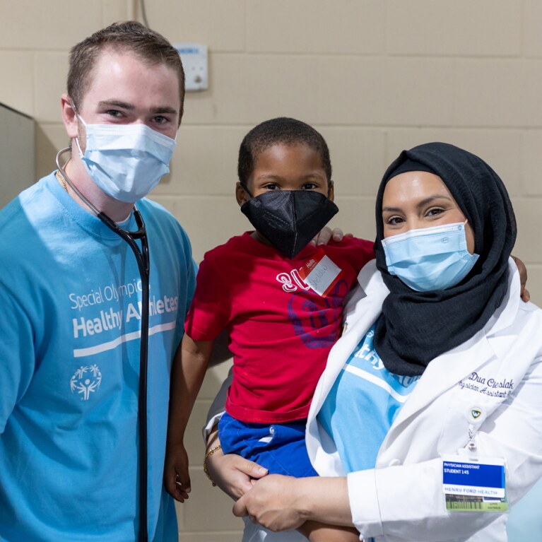 Medical professional holding a young boy, another medical professional stands next to them. 